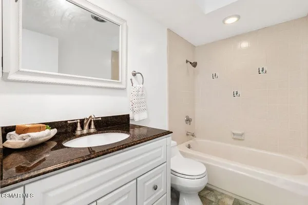 a bathroom with a granite countertop sink and a mirror with bathtub