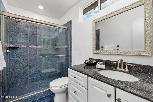 a bathroom with a granite countertop sink a toilet a mirror and shower