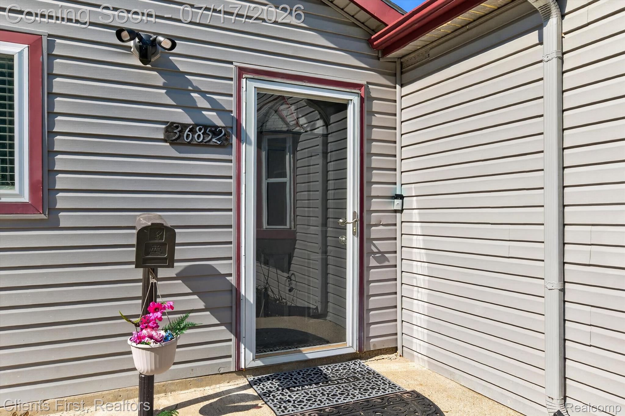 36852 Chase Street Romulus, MI 48174 - Photo 2 of 40 Exterior entry featuring light-colored horizontal siding, a red-trimmed storm door, a wall-mounted light fixture, and visible house numbers