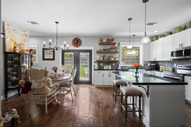 a kitchen with stainless steel appliances kitchen island granite countertop a stove a refrigerator a kitchen island a dining table and chairs with wooden floor
