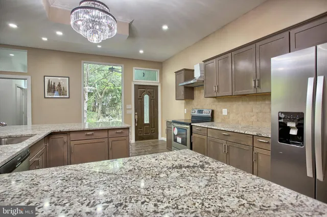 a kitchen with stainless steel appliances granite countertop a sink a stove top oven a counter space and living room view