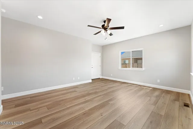 a view of empty room with wooden floor and fan