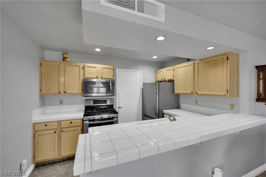 7570 West Flamingo Road, Unit 115 Las Vegas, NV 89147 - Photo 7 of 34 A well-lit kitchen with natural wood cabinetry and a functional tile countertop island.