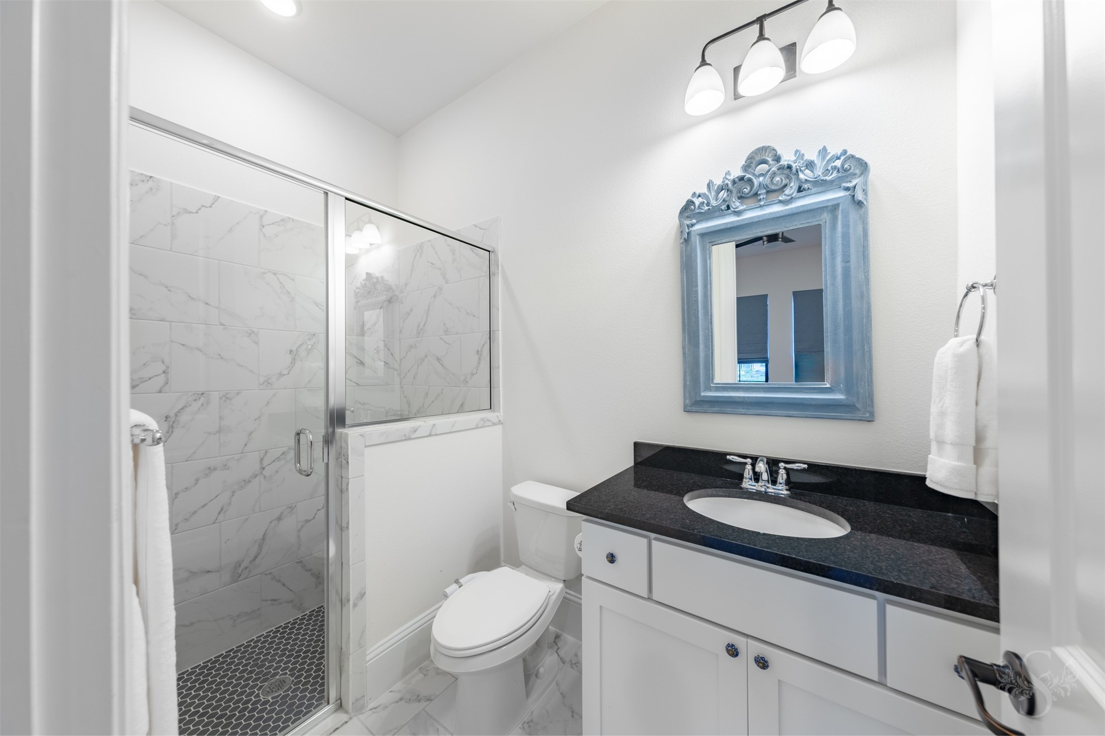 27919 Indigo Ridge Drive Fulshear, TX 77441 - Photo 32 of 50 This beautifully finished ensuite secondary bathroom features a marble-look tiled shower with a framed glass enclosure and a classic black granite vanity. Soft lighting, polished fixtures, and timeless details create a bright, refined space your guests will love.