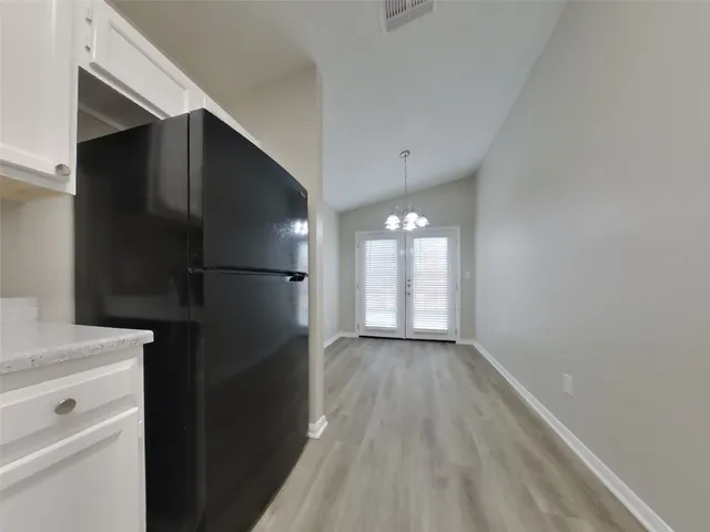 a view of a refrigerator in kitchen and an empty room with wooden floor