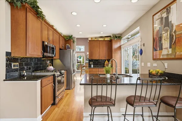 a kitchen with stainless steel appliances granite countertop a stove top oven a sink a refrigerator and chairs