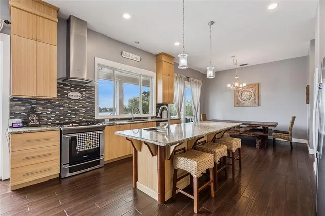 a very nice looking kitchen with granite countertop a stove a sink a refrigerator and white cabinets with wooden floor