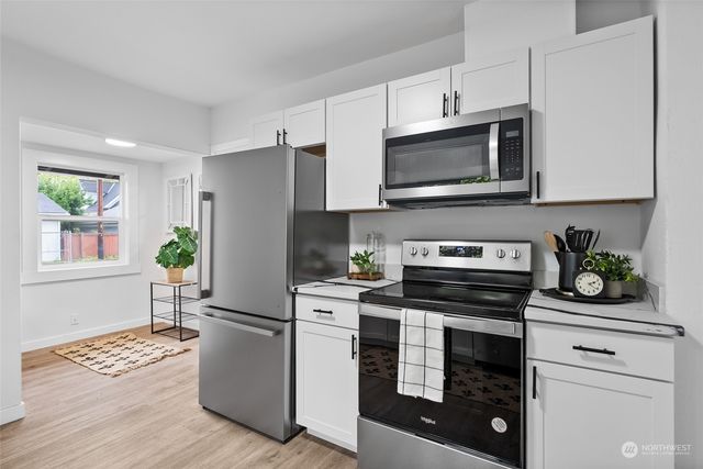 a kitchen with stainless steel appliances white cabinets a stove a microwave a sink and wooden floor