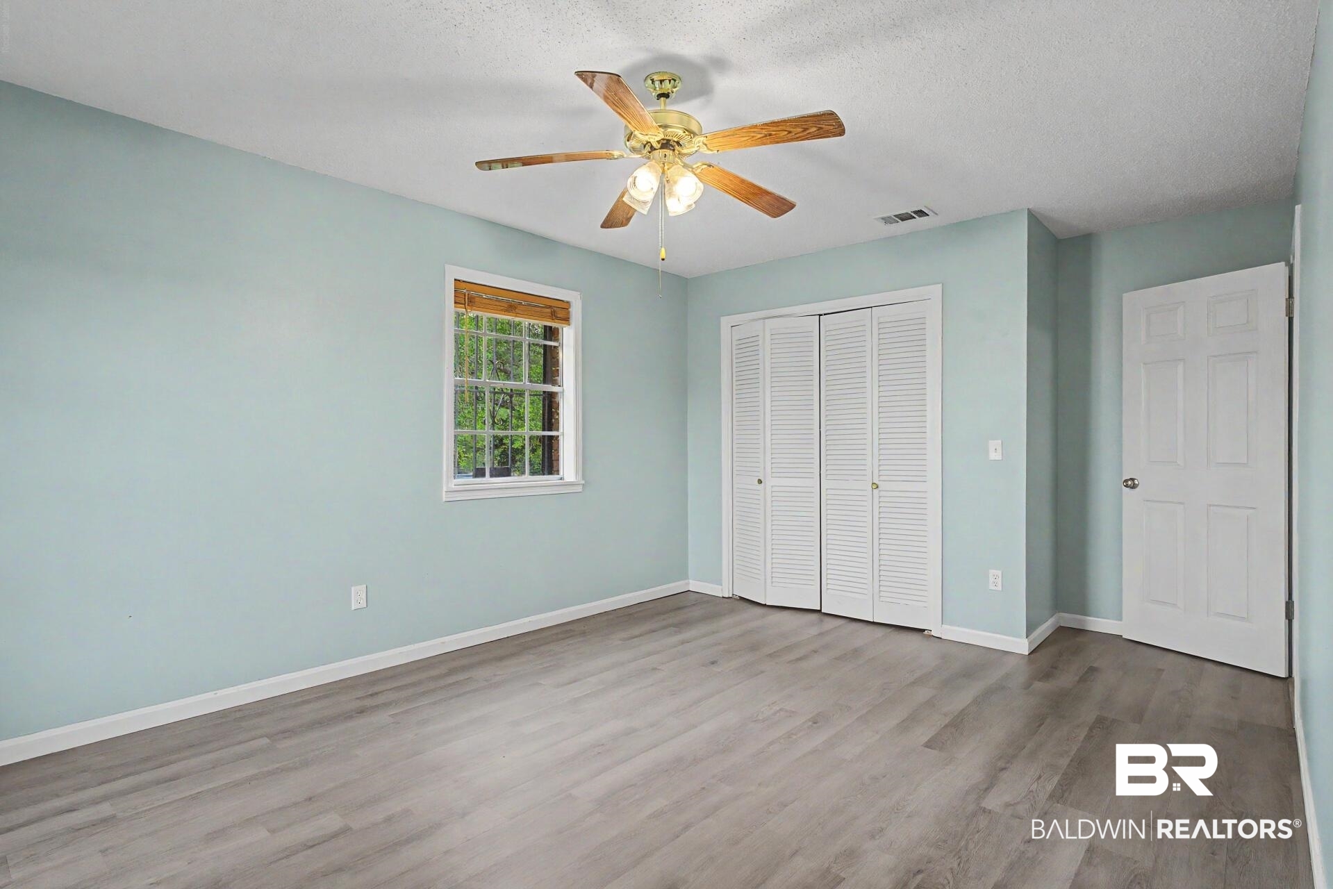 3791 Robinsonville Road Atmore, AL 36502 - Photo 41 of 47 Spacious room featuring wood-finish flooring, a ceiling fan with light fixture, louvered bi-fold closet doors, a window with wood blinds, and a paneled door