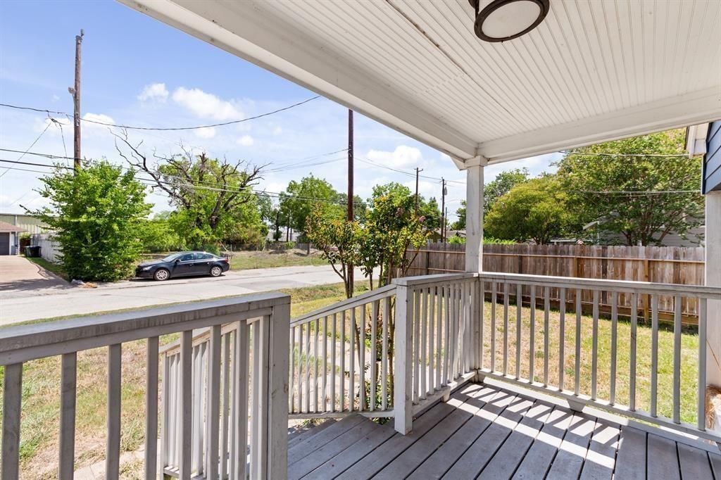 1305 Idylwild Street Houston, TX 77009 - Photo 3 of 31 This photo shows a cozy front porch with a white railing and a view of a quiet street. The porch is covered, providing shade, and overlooks a grassy area with some trees and a wooden fence. Perfect for relaxing outdoors.