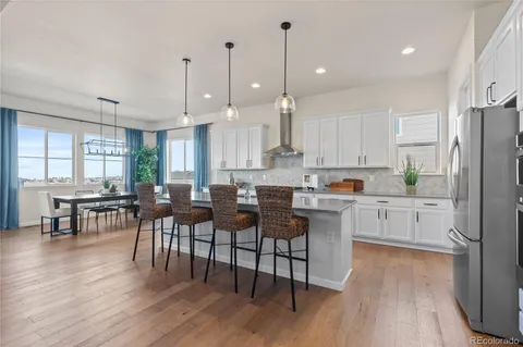 a kitchen with stainless steel appliances granite countertop a stove a refrigerator a kitchen island a dining table and chairs with wooden floor