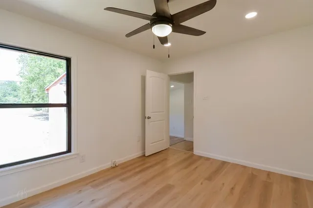 an empty room with wooden floor fan and windows