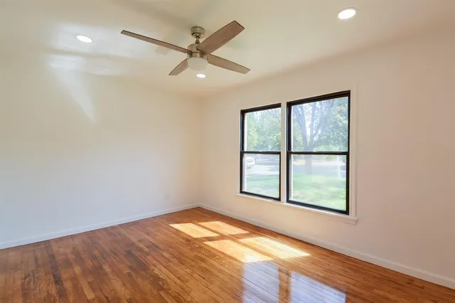 an empty room with wooden floor fan and windows