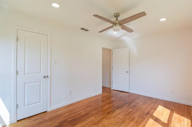 a view of an empty room with wooden floor and a ceiling fan