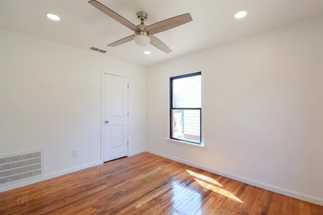 an empty room with wooden floor ceiling fan and windows