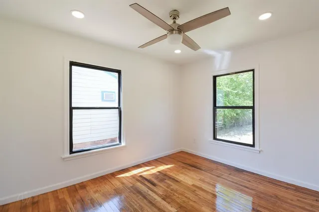 an empty room with wooden floor ceiling fan and windows