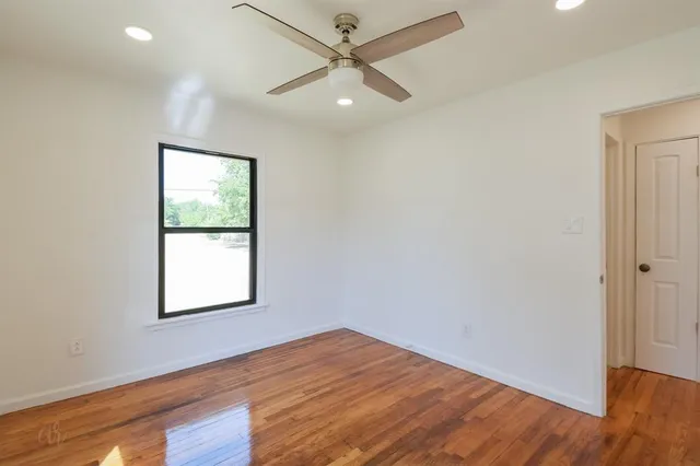 an empty room with wooden floor ceiling fan and windows