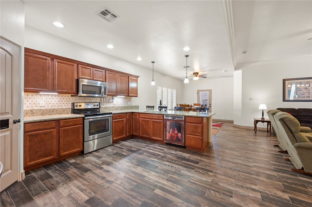 3319 Motherload Road Kingman, AZ 86401 - Photo 9 of 53 Kitchen featuring stainless steel appliances, brown cabinets, decorative light fixtures, plank tile flooring, granite counter tops and recess lighting