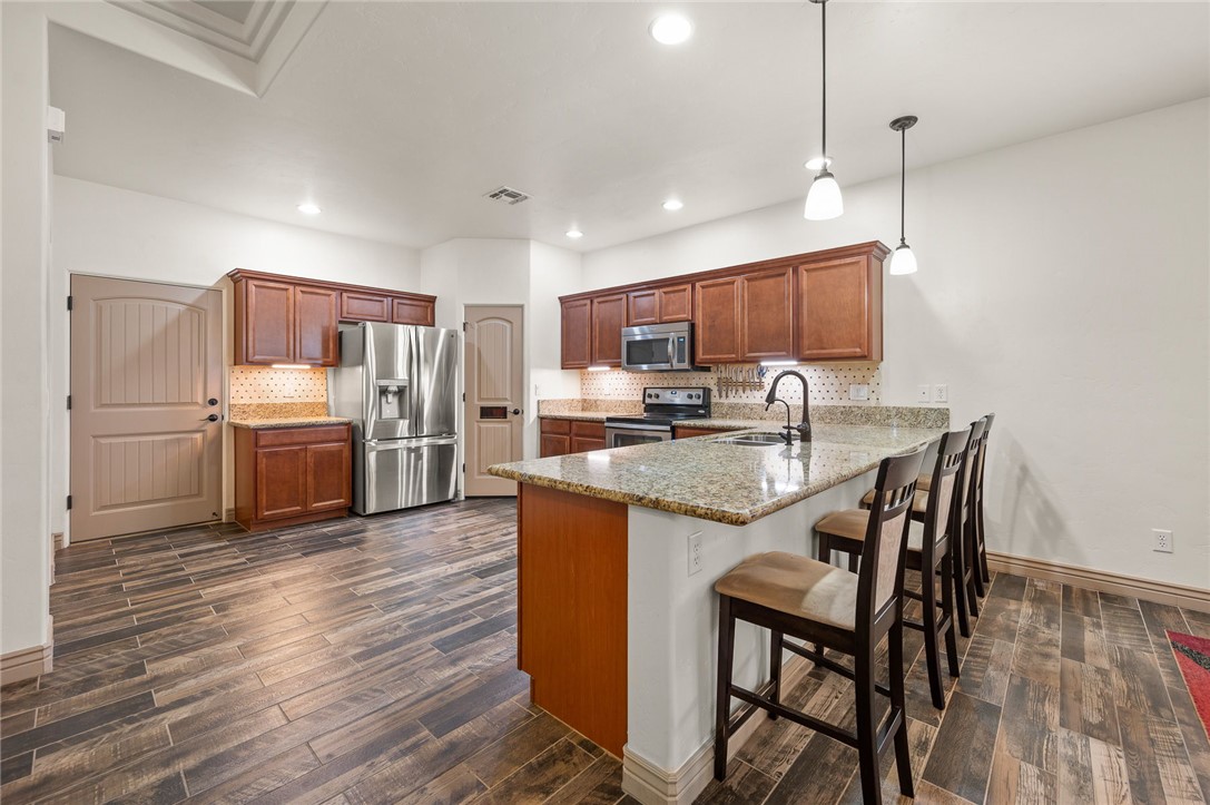 3319 Motherload Road Kingman, AZ 86401 - Photo 7 of 53 Kitchen featuring stainless steel appliances, a peninsula, plank tile flooring, backsplash, and a breakfast bar