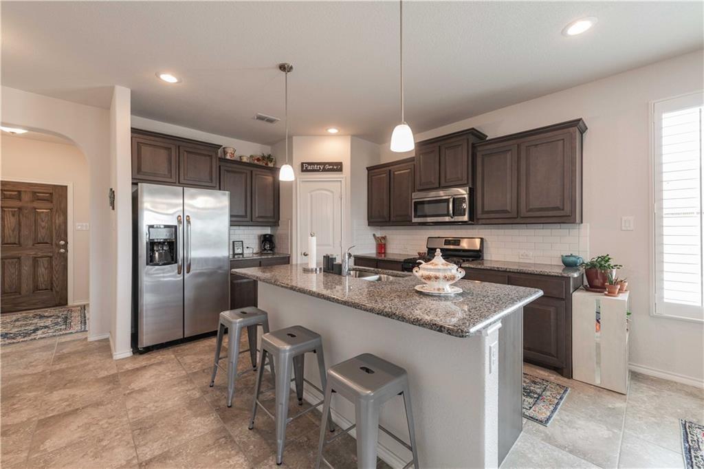 1716 Rio Penasco Road Fort Worth, TX 76052 - Photo 12 of 31 Modern kitchen featuring dark wood cabinetry, granite countertops, stainless steel appliances including a side-by-side refrigerator and built-in microwave, a large center island with seating for three, and pendant lighting