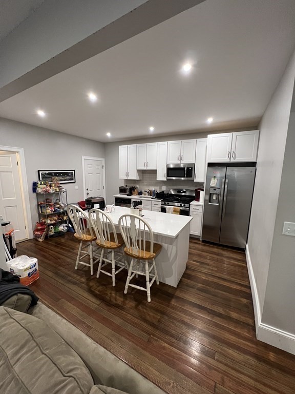 a living room with stainless steel appliances furniture wooden floor and a kitchen view