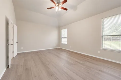 an empty room with wooden floor fan and windows