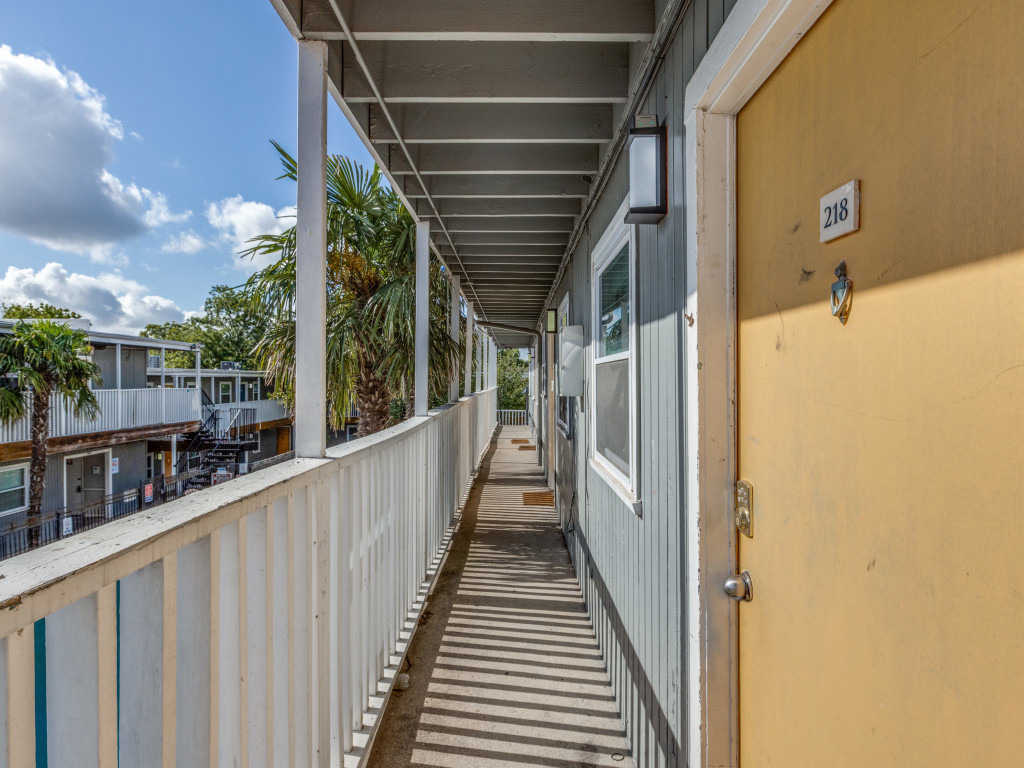 2401 Manor Road, Unit 218 Austin, TX 78722 - Photo 13 of 27 An inviting covered walkway provides sheltered access to residential units, overlooking palm trees and distant structures.