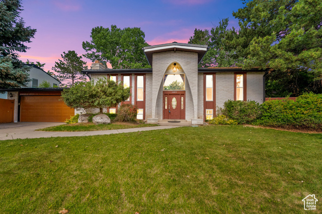 Mid-century home featuring an attached garage, a front lawn, concrete driveway, brick siding, and a chimney