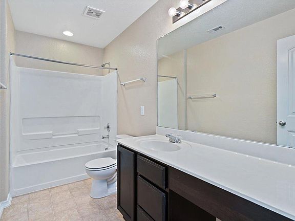 904 Lonesome Lilly Way Pflugerville, TX 78660 - Photo 23 of 34 The bathroom features a vanity with a white countertop and a dark wood cabinet, a large mirror, a toilet, and a combined bathtub and shower unit