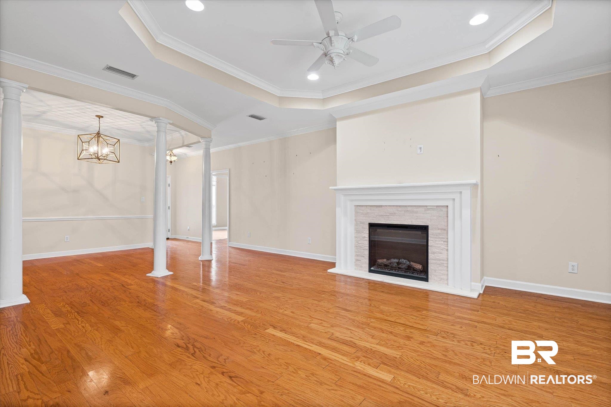 1003 Weatherby Street South Saraland, AL 36571 - Photo 10 of 31 Unfurnished living room with suspended lighting, a tray ceiling, light wood-style floors, a stone fireplace, and ornamental molding