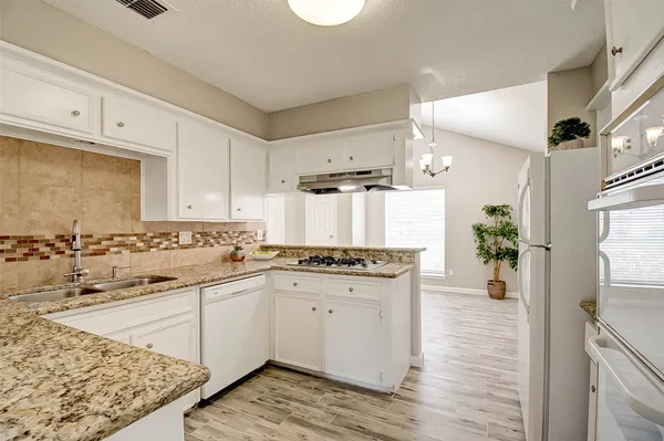 a kitchen with a sink stove and white cabinets with wooden floor