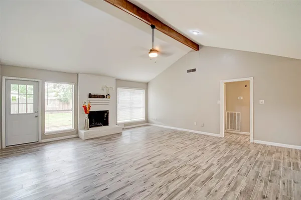 an empty room with wooden floor fireplace and windows