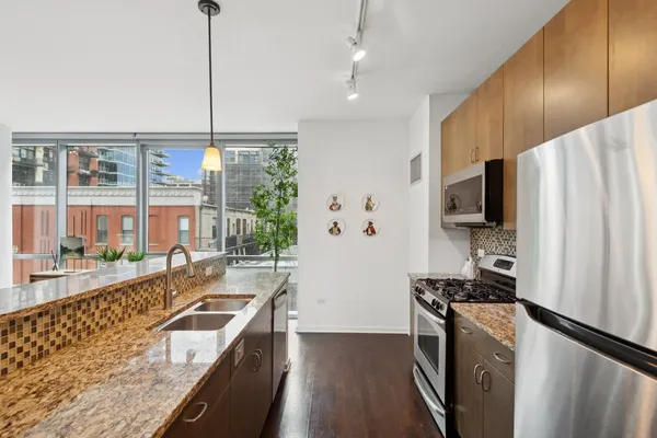 a kitchen with stainless steel appliances granite countertop a refrigerator a stove and a sink with wooden floor
