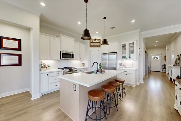 a open kitchen with stainless steel appliances granite countertop a stove top oven a refrigerator a sink and white cabinets with wooden floor