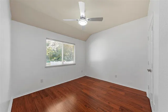 an empty room with wooden floor chandelier fan and windows