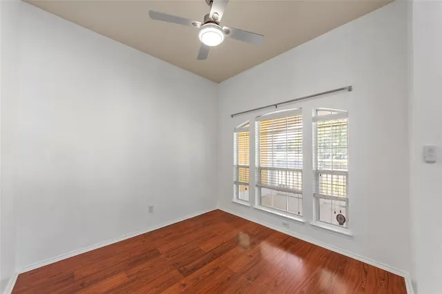 an empty room with wooden floor fan and windows