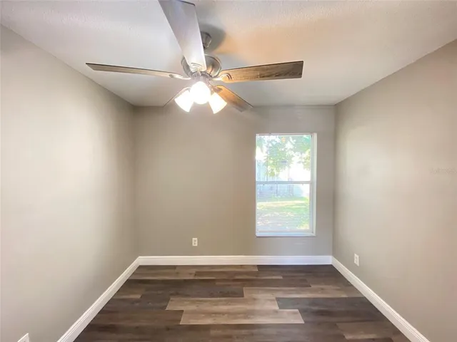 an empty room with wooden floor fan and windows