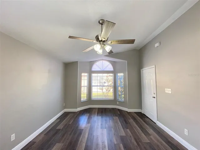 a view of an empty room with wooden floor and fan