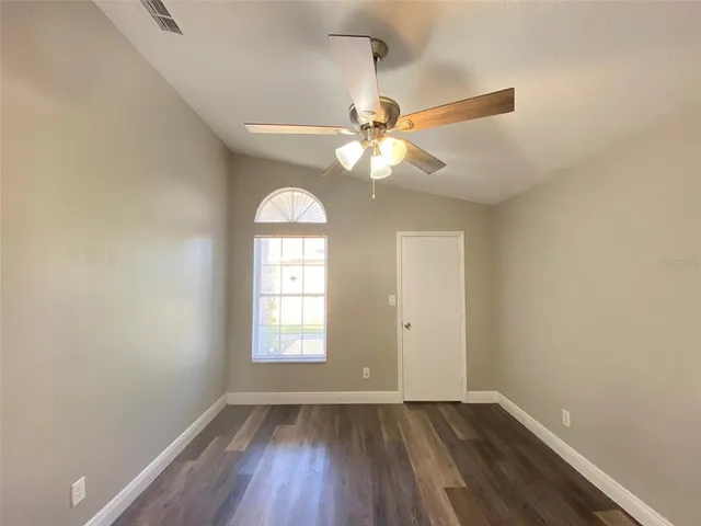 an empty room with wooden floor fan and window