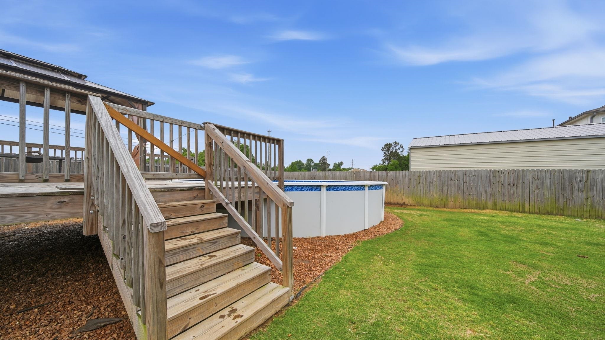 70 Trinity Cove Atoka, TN 38004 - Photo 23 of 25 Expansive backyard featuring a wood deck with stairs, an above-ground pool, a manicured lawn, a wood fence, and a storage structure with a metal roof