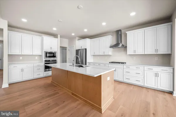 a large kitchen with stainless steel appliances granite countertop a stove top oven a refrigerator a sink and white cabinets with wooden floor