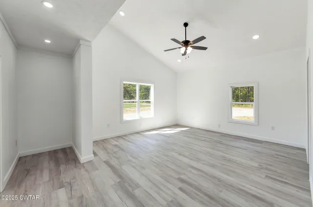 an empty room with wooden floor ceiling fan and windows