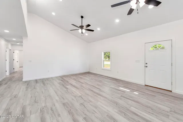 an empty room with wooden floor chandelier fan and windows