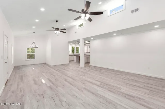 an empty room with wooden floor ceiling fan and windows