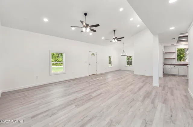 an empty room with wooden floor a ceiling fan and windows