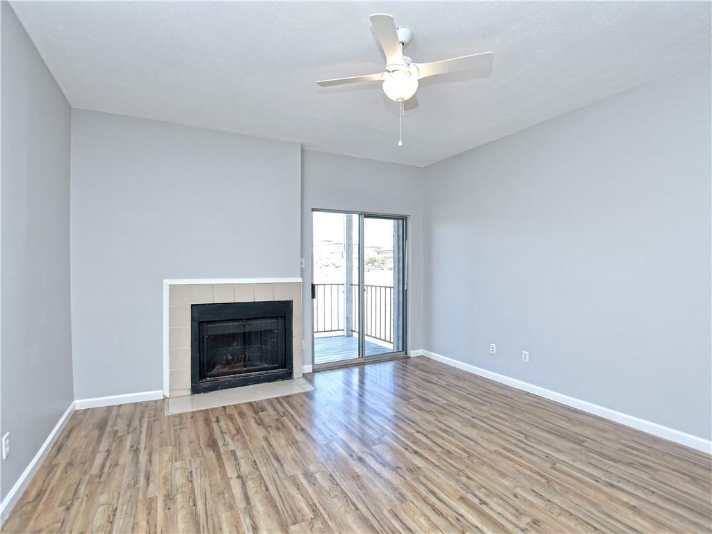 12166 Metric Boulevard, Unit 2015 Austin, TX 78758 - Photo 3 of 18 an empty room with wooden floor a fireplace a ceiling fan and wooden floor