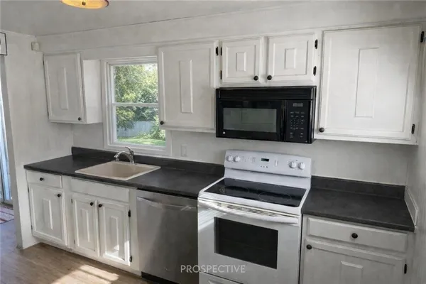 a kitchen with granite countertop white cabinets and a stove a sink with dishwasher and wooden cabinets