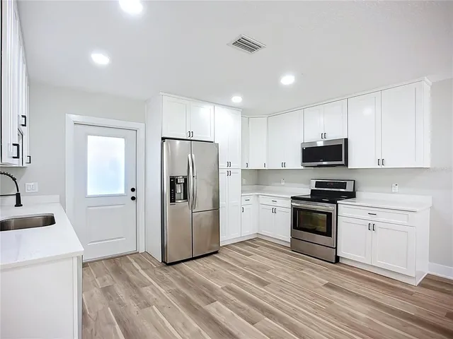 a large kitchen with a lot of white cabinets stainless steel appliances