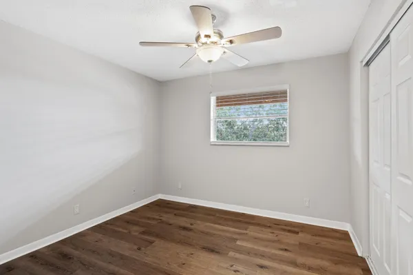 an empty room with wooden floor chandelier fan and windows