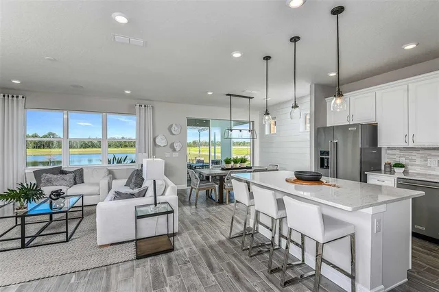 a open kitchen with stainless steel appliances granite countertop a stove a refrigerator a kitchen island a dining table and chairs with wooden floor